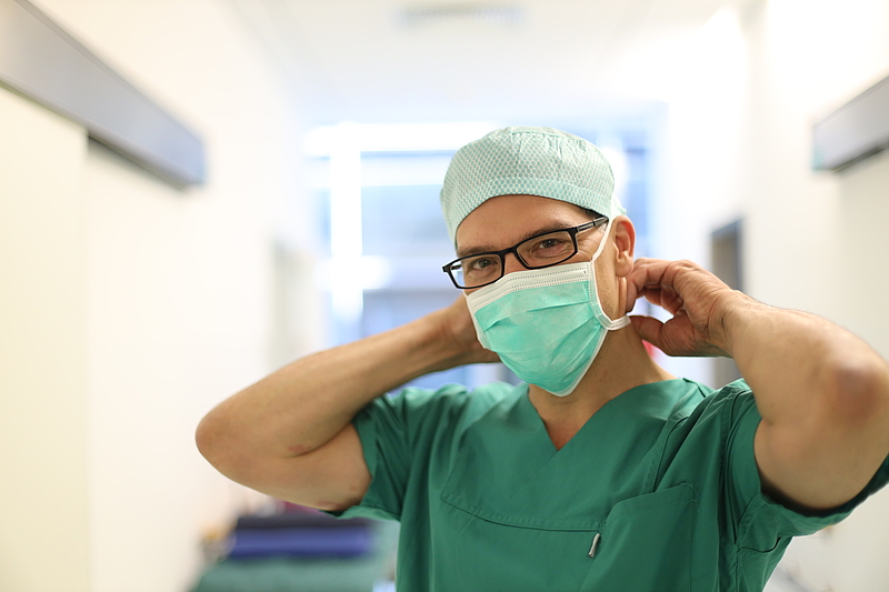 Arzt in OP-Kleidung bindet sich Mundschutz um